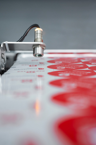 Sensor inspecting substrate behavior during material testing at BERHALTER Swiss Die-Cutting.